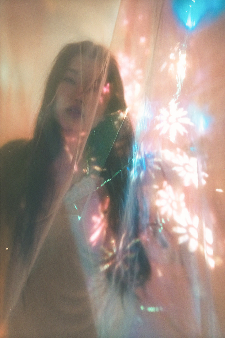 Ambyr beside a sheer curtain with warm projected flowers and a blue balloon.