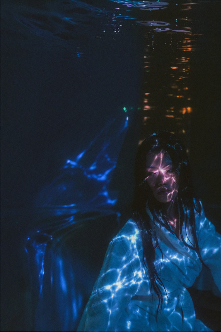 Ambyr in a blue-lit room with shimmering projected patterns across the scene.