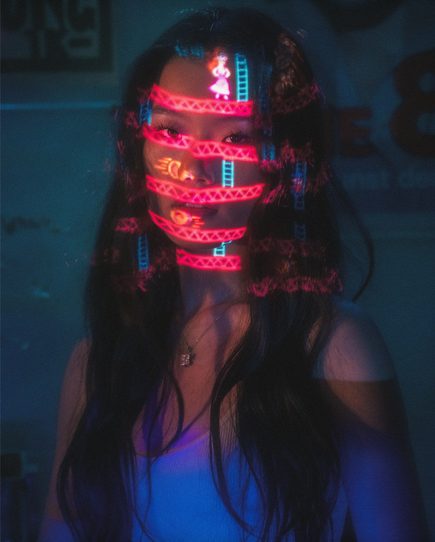 Ambyr with a red illuminated pattern across her face in a blue-lit room.