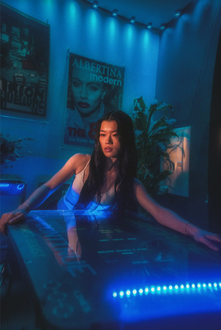 Ambyr with her arms extended across a glass table edged with blue lights.