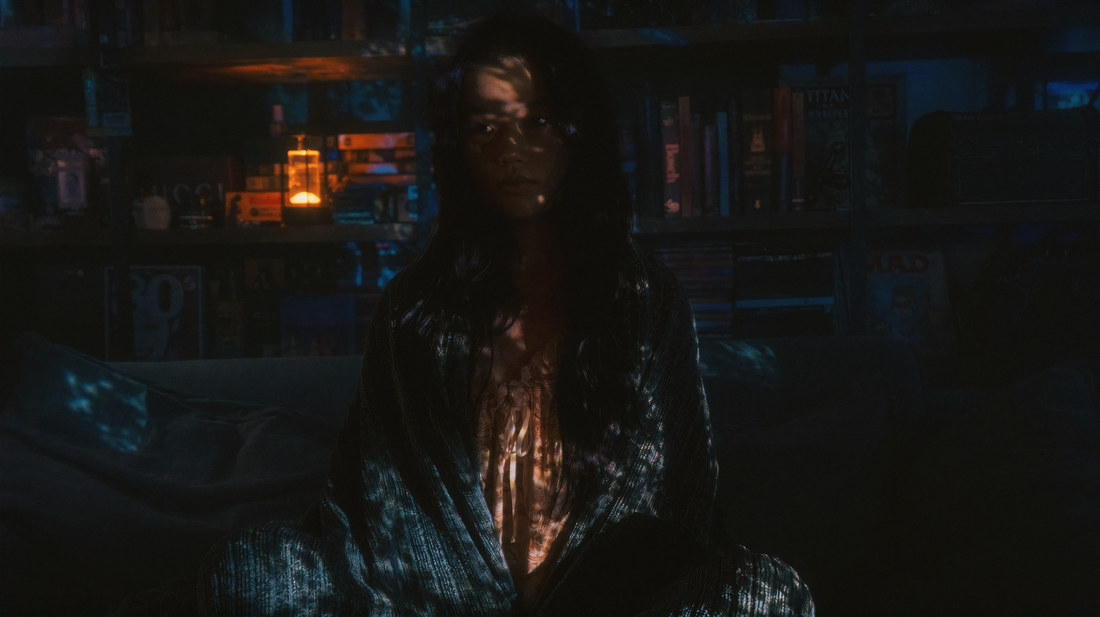 Horizontal portrait of Ambyr seated before bookshelves with warm light across her face.