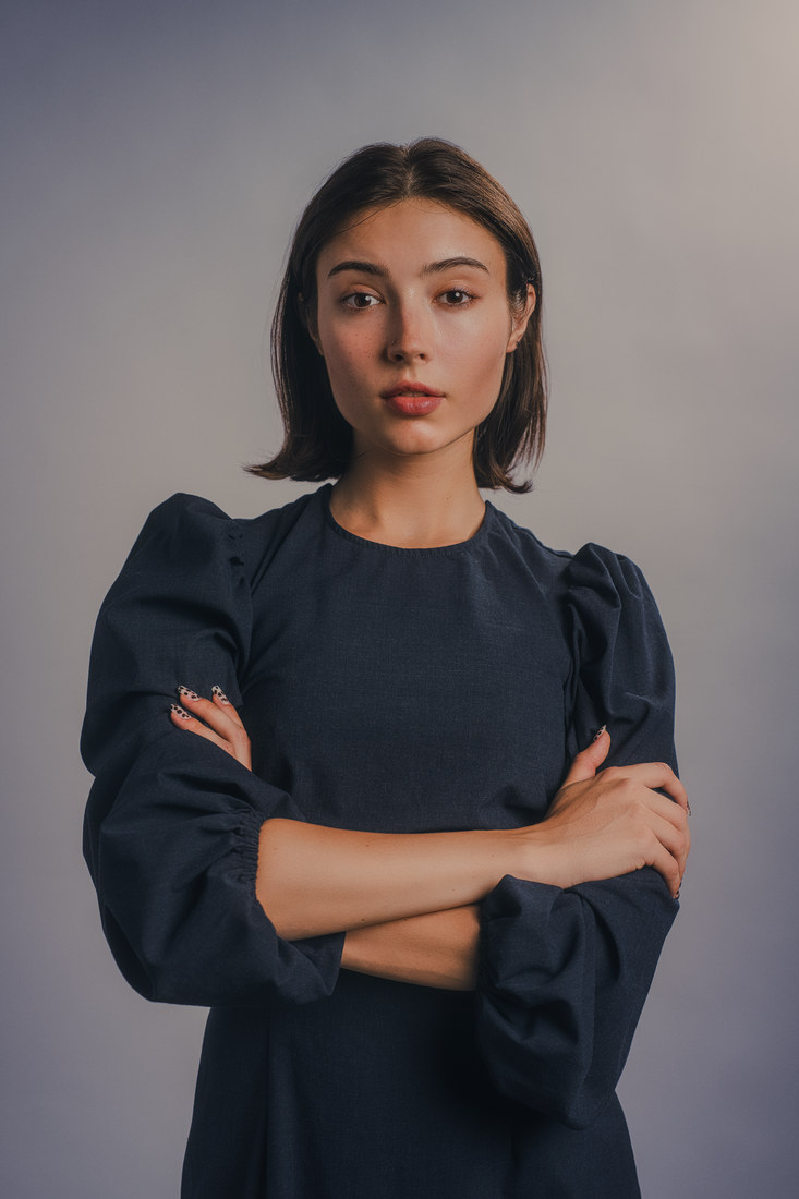 Alla standing with folded arms in a dark puff-sleeve dress.