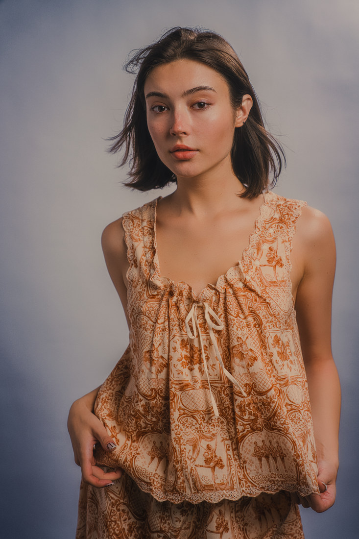 Alla seated in a textured peach sleeveless top against a neutral studio backdrop.