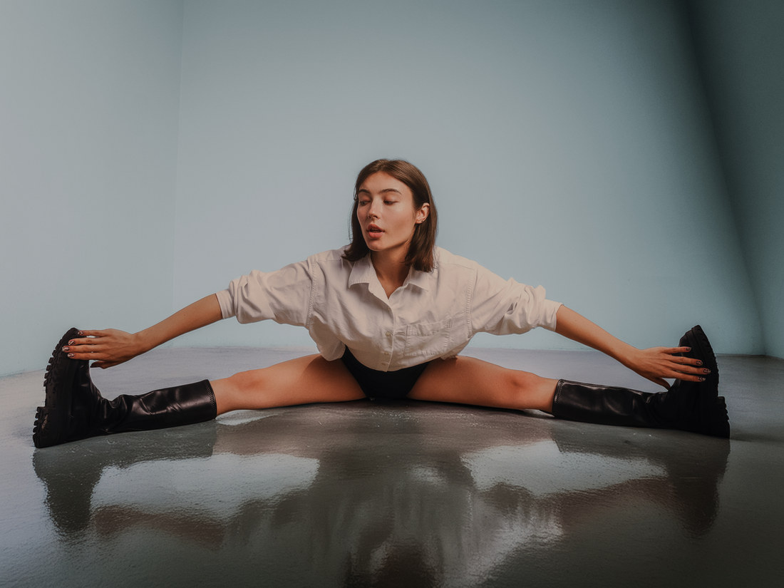 Wide portrait of Alla seated on a reflective studio floor with her legs extended to either side.