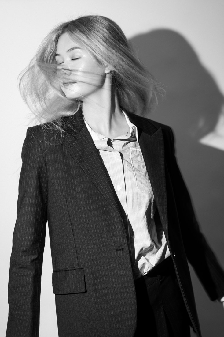 Black-and-white portrait of a model in a suit turning her head, with a shadow behind her.