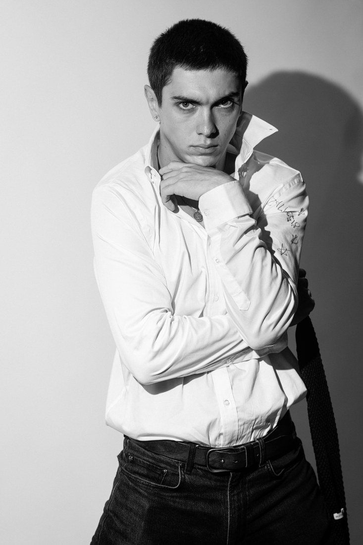 Black-and-white portrait of a model in a white shirt and tie resting his chin on his hands.