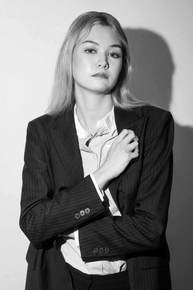 Black-and-white portrait of a model in a dark blazer holding one hand near her collar.