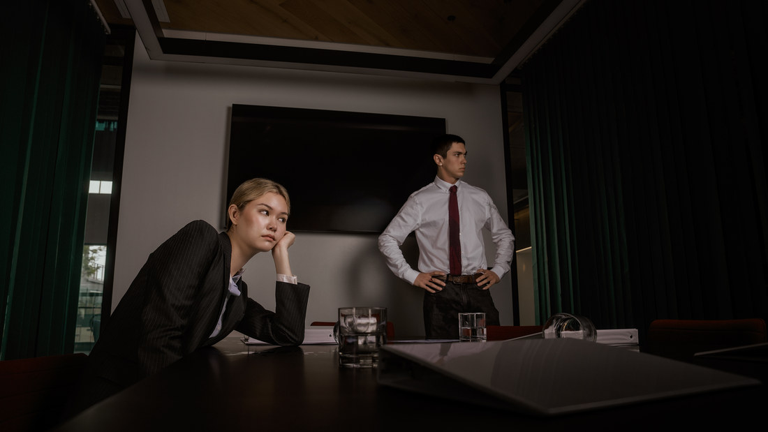 Two models in office attire beside a meeting-room table in a wide interior scene.